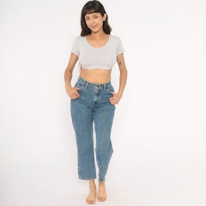 May include: A light gray crop top and blue jeans. The crop top has a scoop neck and short sleeves. The jeans are high-waisted with a straight leg. The model is standing in front of a white background.