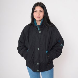 May include: Black jacket with teal accents, featuring a high collar and button closure. The jacket has teal pockets and cuffs, and decorative details on the sleeves. A casual outerwear piece.