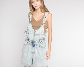 May include: A light blue denim overall short with a zipper closure and a brown tank top underneath.