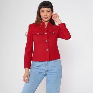 May include: A red blazer with a mandarin collar and silver buttons. The blazer has two flap pockets on the front and a fitted silhouette.