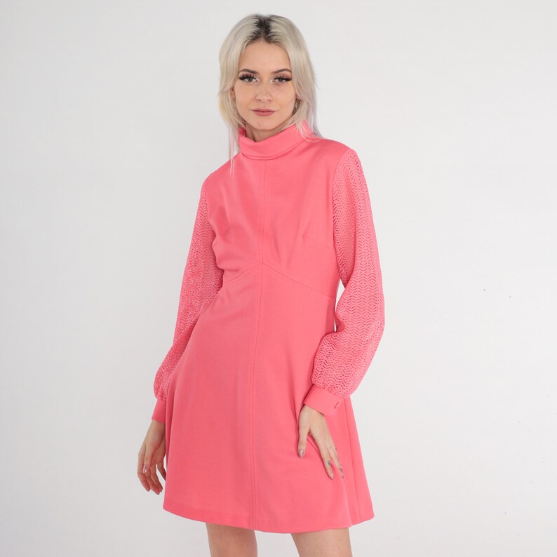May include: A pink dress with a high neck and long sleeves. The sleeves are made of a lacy material. The dress has a fitted bodice and a flared skirt.