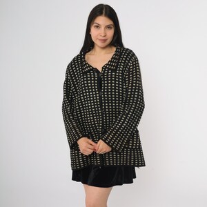 May include: A black and beige checkered cardigan with a collared neckline and a zipper closure. The cardigan is knee-length and has long sleeves. The woman is wearing a black velvet skirt.