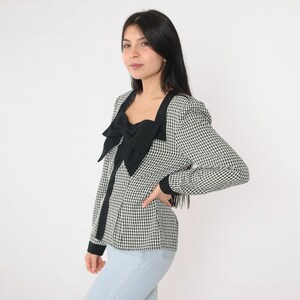 May include: A black and white gingham blouse with a large black bow at the neckline. The blouse has long sleeves and a fitted silhouette.