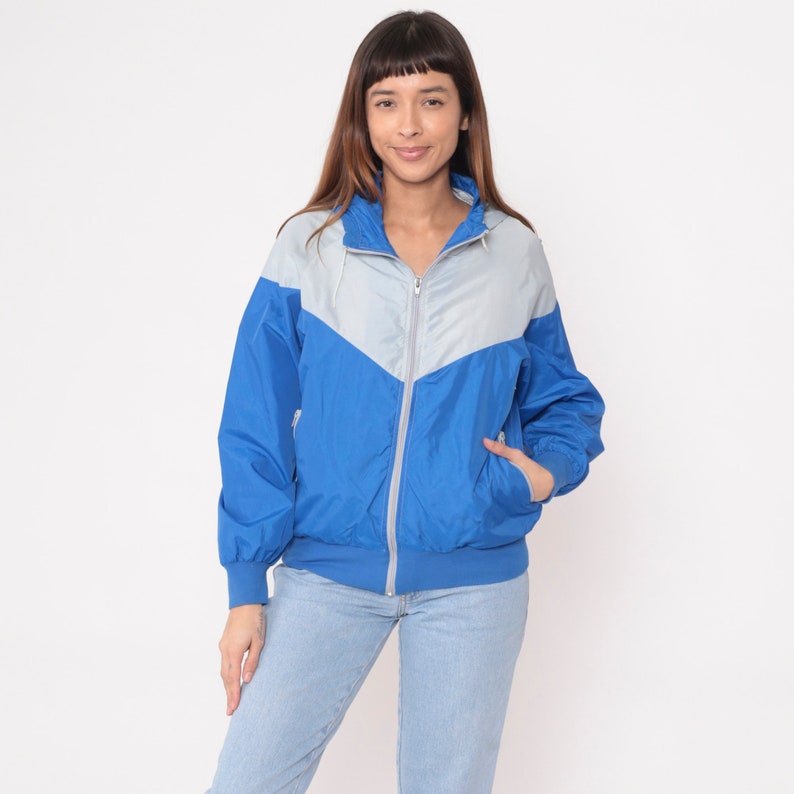 May include: A blue and gray color block windbreaker jacket with a zipper closure and a hood.