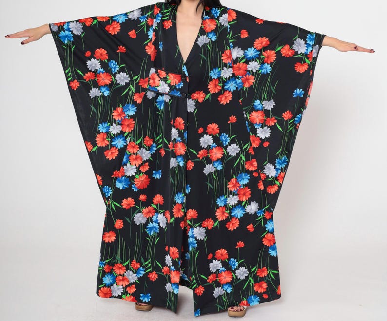 May include: A black kimono with a floral print featuring red, blue, and white flowers. The kimono has long sleeves and a wide, flowing silhouette.