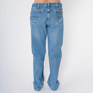 Pu&ograve; includere: Un paio di jeans blu denim a gamba dritta. I jeans hanno un design classico a cinque tasche e una toppa in pelle sul retro della cintura.