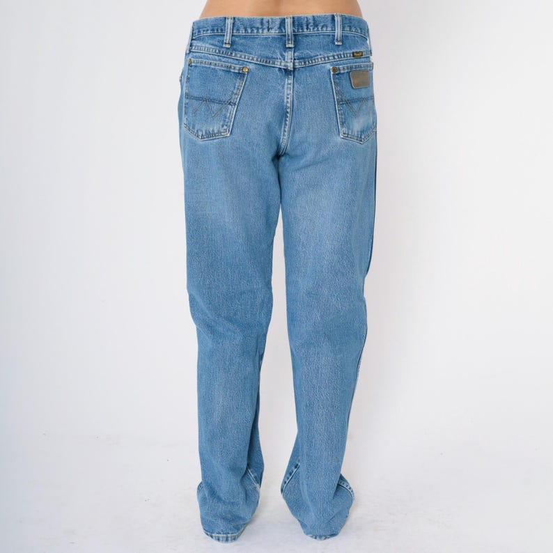 Pu&ograve; includere: Un paio di jeans blu denim a gamba dritta. I jeans hanno un design classico a cinque tasche e una toppa in pelle sul retro della cintura.