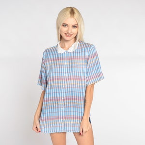 May include: A short-sleeved, button-down shirt with a blue, pink, and yellow plaid pattern. The shirt features a white, scalloped collar. The garment is made of a lightweight fabric, suitable for warm weather.
