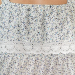 May include: White sleeveless top with a blue floral print and a white lace trim.