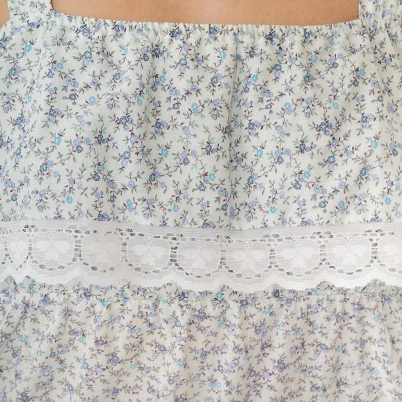 May include: White sleeveless top with a blue floral print and a white lace trim.