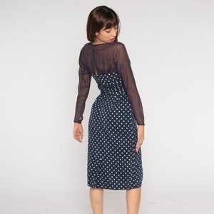 May include: A navy blue midi dress with white polka dots and a sheer black overlay. The dress has long sleeves and a fitted bodice.