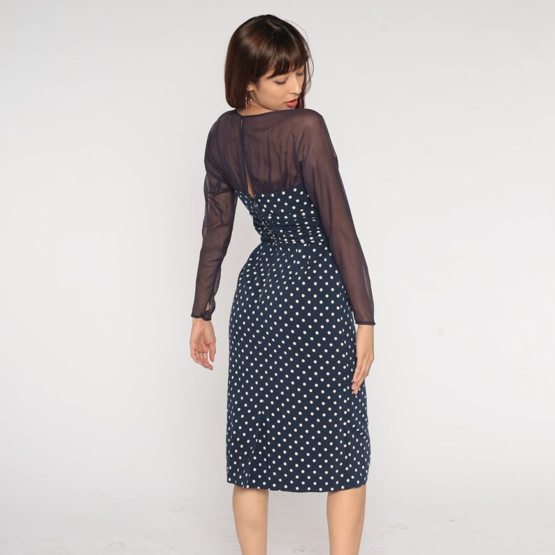 May include: A navy blue midi dress with white polka dots and a sheer black overlay. The dress has long sleeves and a fitted bodice.
