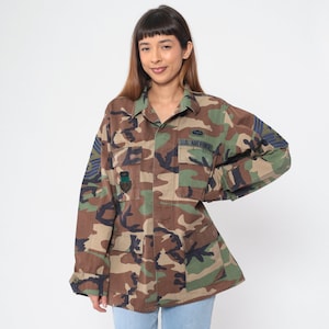 May include: A camouflage jacket with a blue patch that says "U.S. AIR FORCE". The jacket has a green patch on the left chest and blue patches on the sleeves.