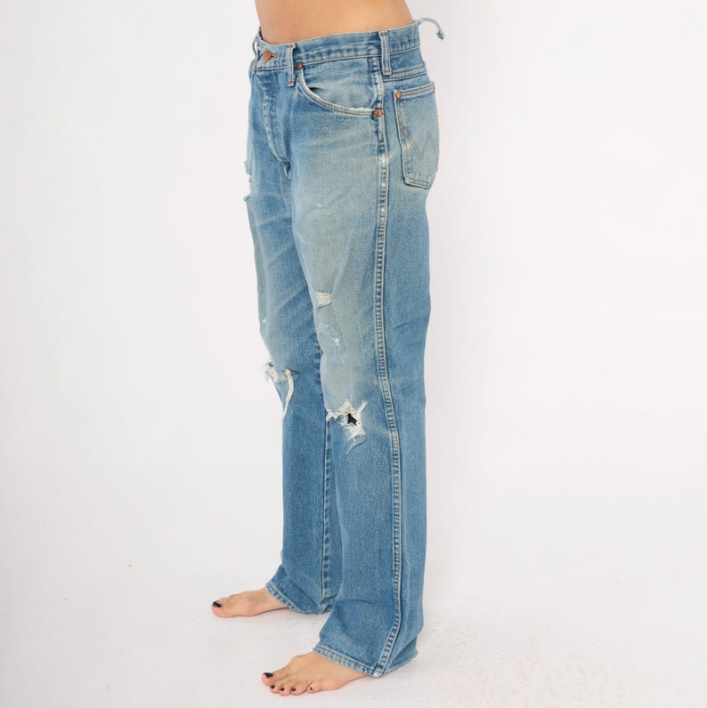 May include: Light blue denim jeans with distressed details, including rips and faded patches. The jeans have a classic five-pocket design and a straight leg fit. The jeans are worn and have a vintage look.