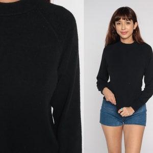 May include: A black long-sleeved sweater with a round neckline and raglan sleeves.