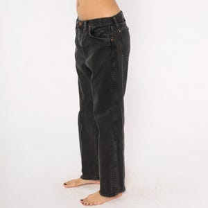 May include: Faded black denim jeans. The jeans have a classic five-pocket design, a button and zipper closure, and a straight leg fit. The jeans are worn and have a slightly distressed look, suggesting they are vintage or have been well-worn.