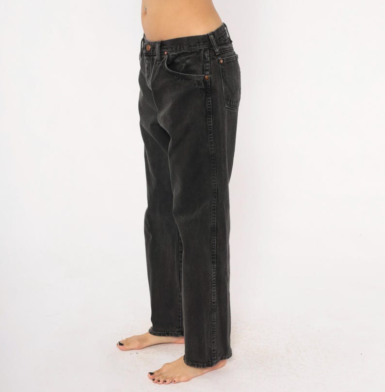 May include: Faded black denim jeans. The jeans have a classic five-pocket design, a button and zipper closure, and a straight leg fit. The jeans are worn and have a slightly distressed look, suggesting they are vintage or have been well-worn.