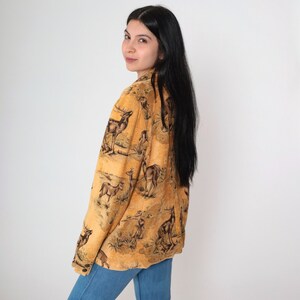 May include: A tan blazer featuring a detailed print of deer and other wildlife. The blazer has a button closure and long sleeves. The overall design is reminiscent of a vintage tapestry, with a classic, nature-inspired theme.