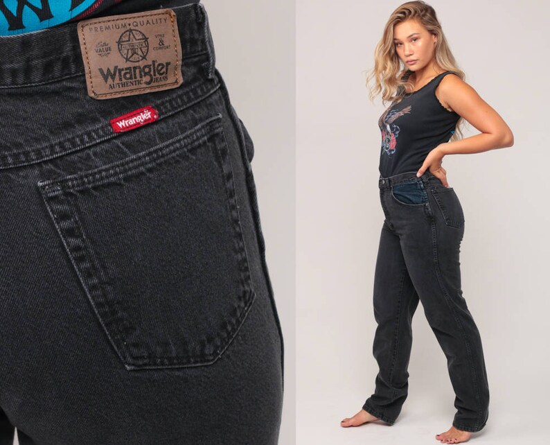 May include: Black Wrangler jeans with a classic fit. The jeans feature a brown leather patch with the Wrangler logo and a red logo tag on the back pocket. The model is wearing a black tank top.