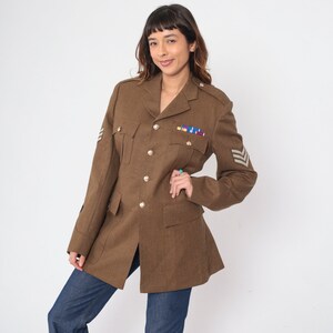 May include: A brown military-style jacket with a double-breasted closure, flap pockets, and a patch on the sleeve with a chevron design.