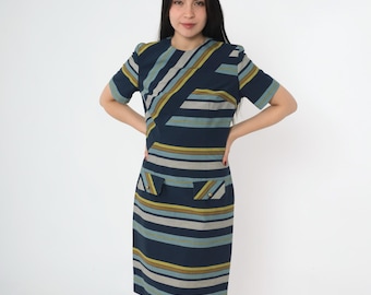 Puede incluir: Un vestido azul marino con un patrón geométrico de rayas y líneas diagonales en tonos de azul, amarillo y gris. El vestido tiene mangas cortas y dos bolsillos de parche en la parte delantera.