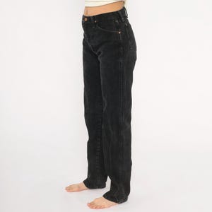 May include: Black denim jeans with a high waist and straight leg. The jeans feature classic five-pocket styling with copper rivets and a button closure. The dark wash denim has a faded appearance, giving a vintage feel.