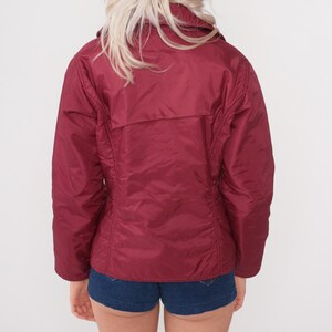 May include: A burgundy-colored jacket with a collared neckline and a zipper closure. The jacket has a quilted appearance and a slightly shiny finish. The back view shows a fitted silhouette, with seams running down the sides and back.