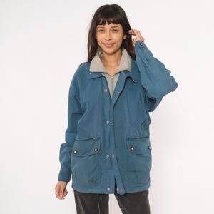 Peut inclure: Veste bleu sarcelle avec un col gris et une chemise grise zippée en dessous. La veste a deux poches avant avec des fermetures à boutons et un devant boutonné. La veste est de style décontracté.