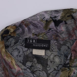 May include: Close-up of a patterned button-down shirt. The fabric features a floral design in shades of grey, green, and pink. The label reads "I&R ILLUSIONS".