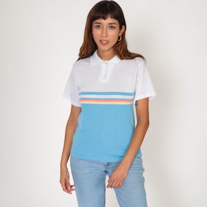 May include: White and light blue polo shirt with a ribbed texture. The shirt features a light blue band across the chest with horizontal stripes of pink, yellow, and orange. The shirt has short sleeves and a collared neckline.