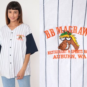 May include: White baseball jersey with navy blue sleeves and vertical pinstripes. The jersey features the embroidered text "BB McGraws Restaurant & Sports Bar Auburn, WA" and a cartoon horse logo on the chest.