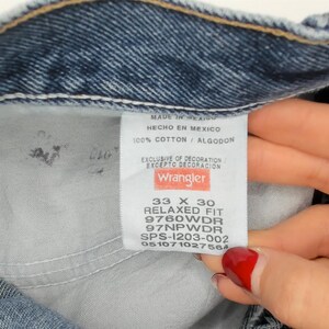 May include: Close-up of a pair of blue denim jeans. The interior label reads "Wrangler" with details including size 33 x 30, relaxed fit, and fabric composition. The jeans are made in Mexico and are 100% cotton.