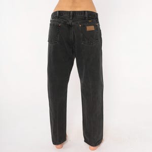 May include: Black denim jeans with a classic five-pocket design. The jeans feature a straight leg cut and a brown leather patch on the back pocket. The jeans are made of a durable denim material.