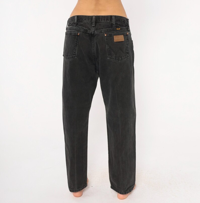 May include: Black denim jeans with a classic five-pocket design. The jeans feature a straight leg cut and a brown leather patch on the back pocket. The jeans are made of a durable denim material.