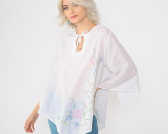 May include: White, loose-fitting blouse with a floral print and a tie at the neckline.