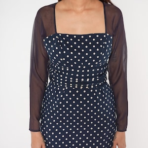 May include: A navy blue dress with white polka dots and sheer black sleeves. The dress has a square neckline and a fitted bodice.
