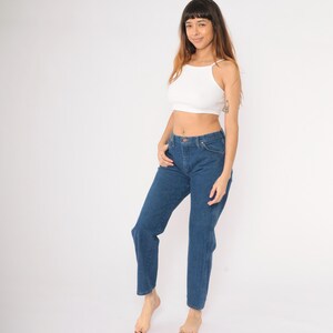 May include: A woman wearing a white crop top and blue denim jeans. The jeans have a high waist and a straight leg.