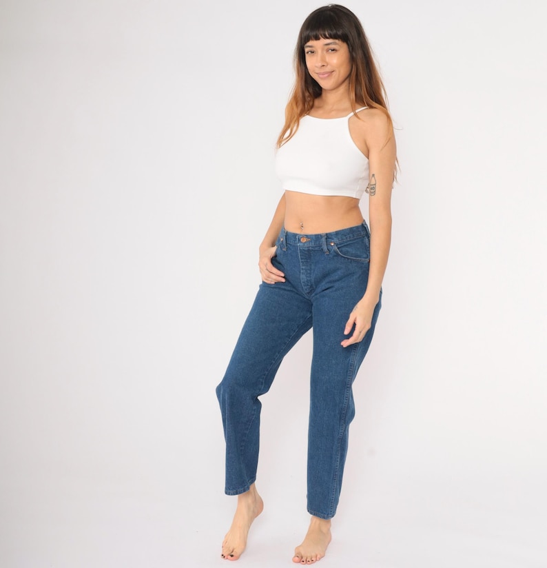 May include: A woman wearing a white crop top and blue denim jeans. The jeans have a high waist and a straight leg.