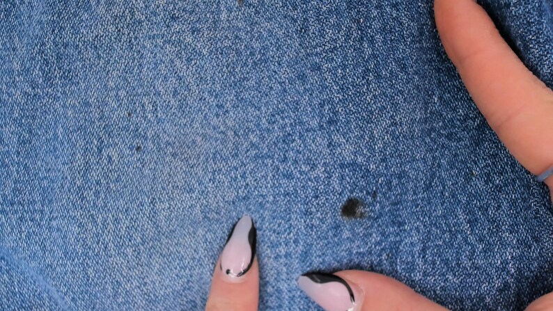 Pode incluir: Close-up de tecido jeans azul com manchas escuras. A textura do jeans &eacute; vis&iacute;vel, mostrando a trama do tecido. A imagem &eacute; bem iluminada, destacando os detalhes do material.