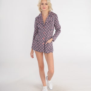 Puede incluir: Una chaqueta gris con estampado floral rosa y rojo. La chaqueta tiene cierre de botones y bolsillos. La modelo lleva zapatillas blancas.