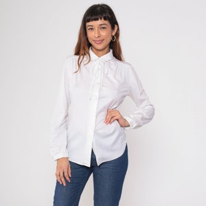 May include: A white long-sleeved button-down shirt with a bow tie collar. The shirt has a relaxed fit and is made of a soft, comfortable fabric.