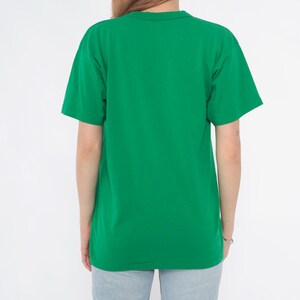 K&ouml;nnte beinhalten: Ein einfarbiges gr&uuml;nes T-Shirt mit kurzen &Auml;rmeln. Die R&uuml;ckansicht des T-Shirts zeigt ein schlichtes, klassisches Design. Das Shirt ist aus einem weichen Material und hat einen leuchtenden Gr&uuml;nton.