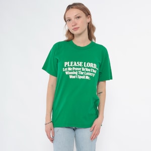 K&ouml;nnte beinhalten: Gr&uuml;nes T-Shirt mit dem Text "PLEASE LORD... Let Me Prove To You That Winning The Lottery Won't Spoil Me." Das Shirt hat einen Rundhalsausschnitt und kurze &Auml;rmel. Die Person tr&auml;gt eine hellblaue Jeans.