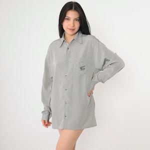 May include: A gray long-sleeved button-down shirt with a small alligator logo embroidered on the left chest pocket.
