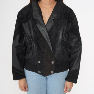 May include: A black leather jacket with a suede trim and a double-breasted closure. The jacket has a textured surface and a slightly oversized fit.