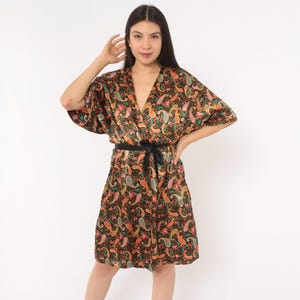 May include: A black satin robe featuring a vibrant, multi-colored paisley print in shades of orange, pink, green, and gold. The garment has a V-neckline, wide short sleeves, and a matching black fabric tie belt at the waist for a secure closure.