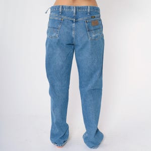 May include: A pair of light blue denim jeans with a brown leather patch on the back pocket that says "Wrangler".
