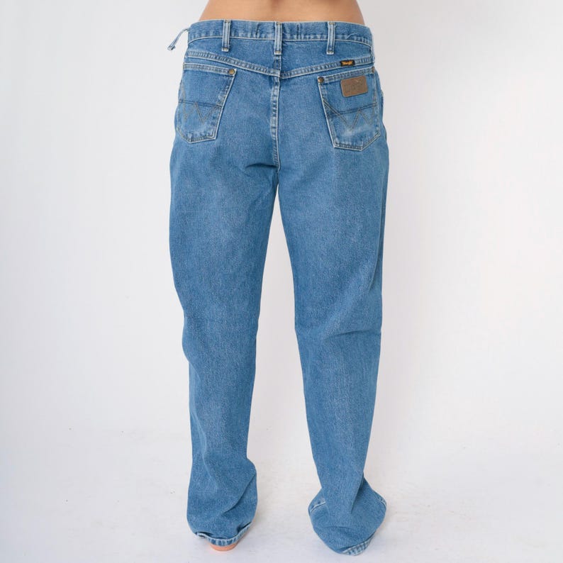 May include: A pair of light blue denim jeans with a brown leather patch on the back pocket that says "Wrangler".
