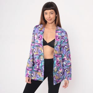 Könnte beinhalten: Ein offener Blazer mit farbenfrohem Muster in Lila, Blau und Gelb. Der Blazer hat ein abstraktes Design. Das Kleidungsstück wird offen getragen und zeigt die inneren Schichten.
