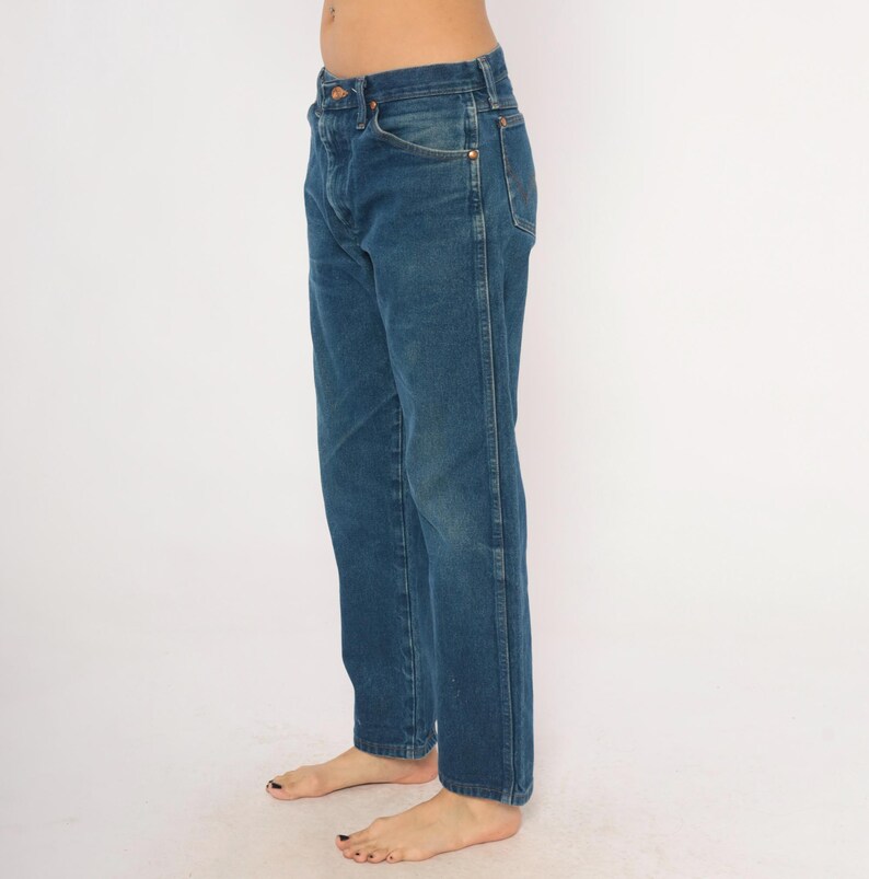 May include: Blue denim jeans with a classic five-pocket design. The jeans have a straight leg cut and a button and zipper closure. The denim has a medium wash with subtle fading and wear marks. The jeans are shown from the side.